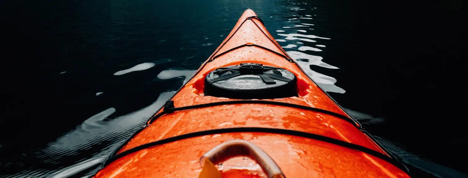 La proue d'un kayak orange sur une eau calme.